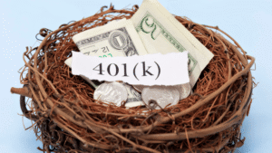 A bird’s nest containing US dollar bills and coins with a torn piece of paper labeled "401(k)" resting on top, symbolizing retirement savings.
