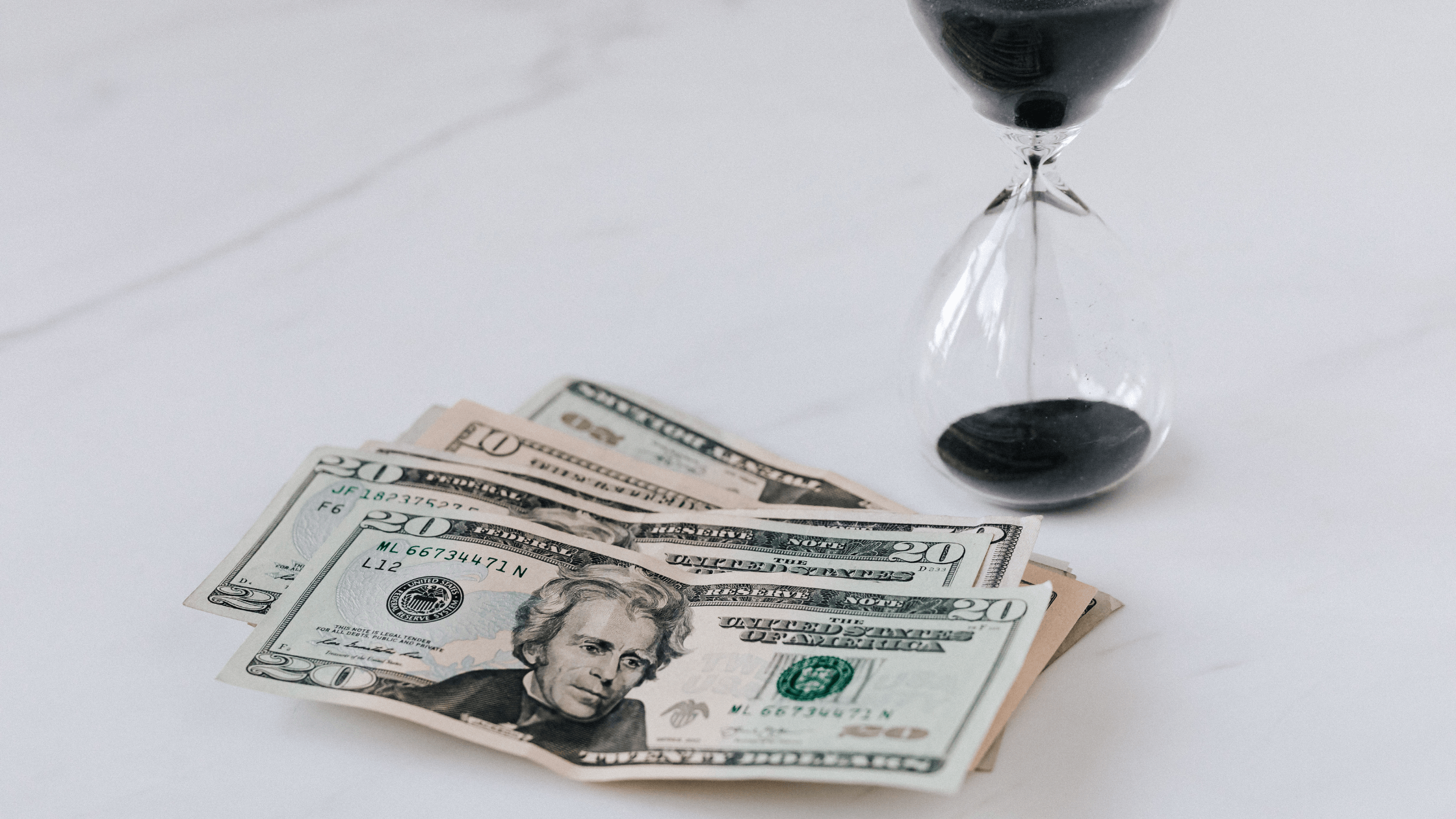 A fan of US twenty and ten-dollar bills next to an hourglass with black sand, symbolizing the limited time window for strategic tax planning.