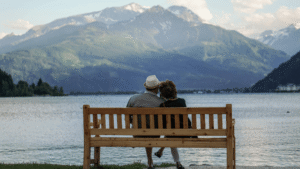 A retired couple sitting on a wooden bench overlooking a serene lake and mountain range, symbolizing the peace of mind that comes with a personalized retirement plan.