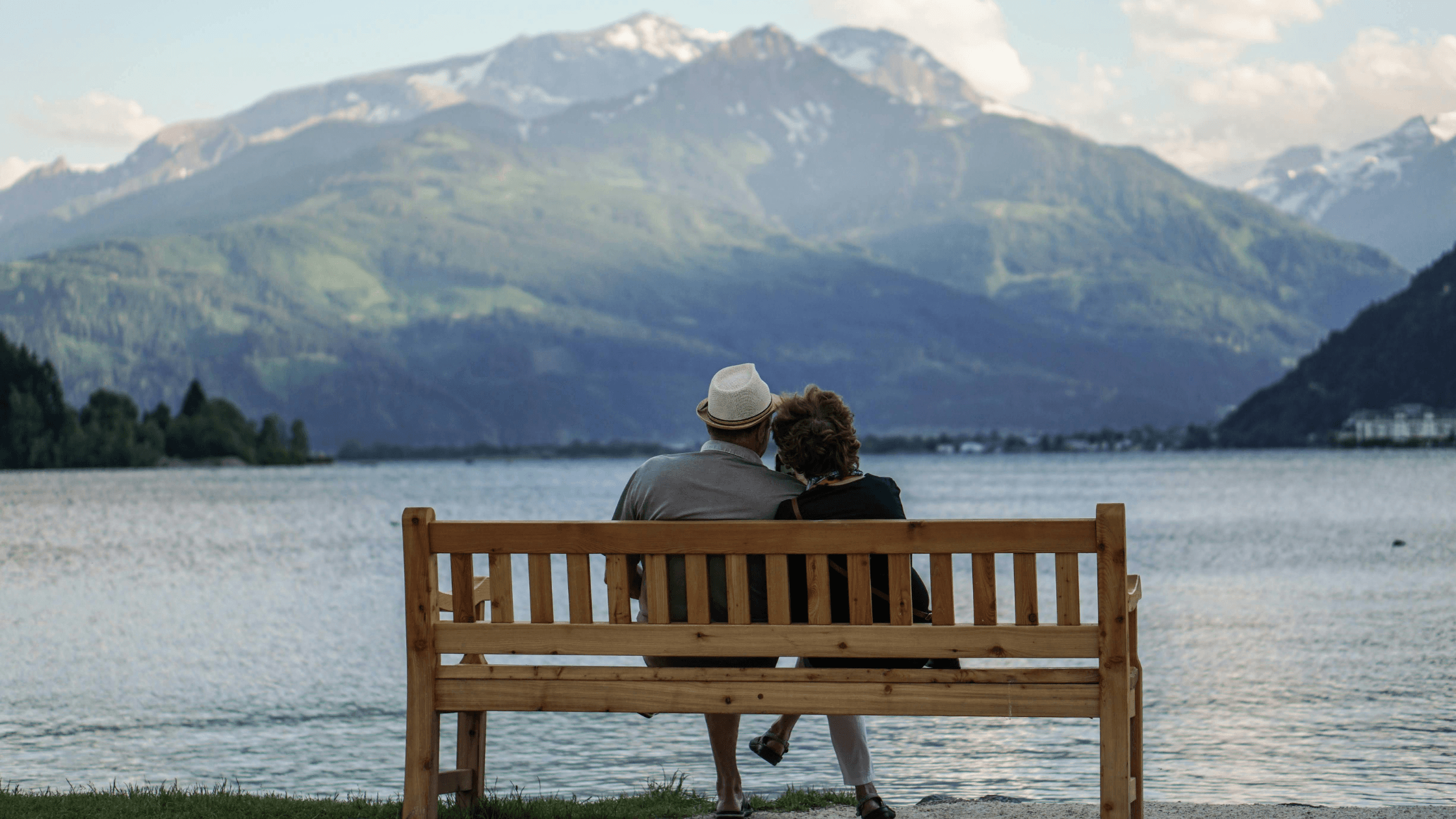 A retired couple sitting on a wooden bench overlooking a serene lake and mountain range, symbolizing the peace of mind that comes with a personalized retirement plan.